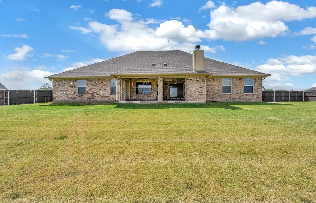 Expansive backyard featuring a manicured lawn, brick exterior, and covered patio