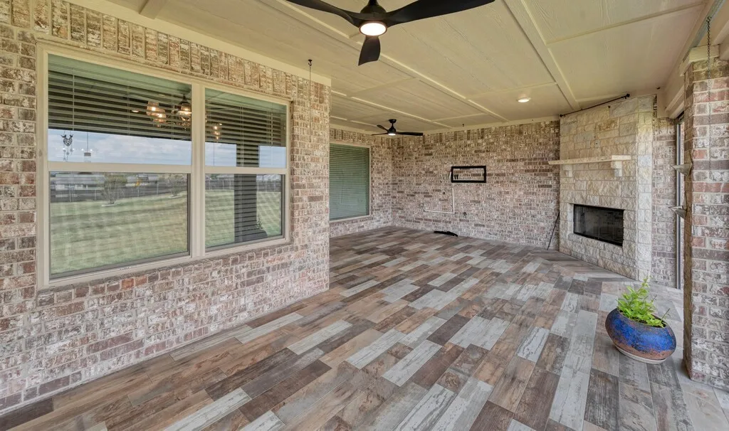 Spacious covered patio with wood-finish plank flooring, ceiling fan, and brick exterior walls, Remote Solar Screens