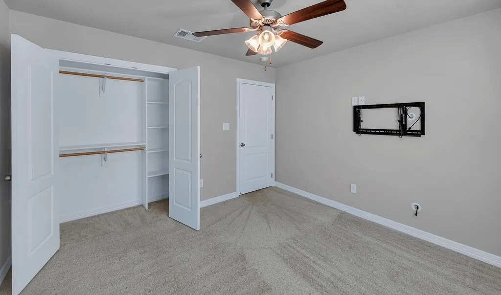 Spacious room featuring carpeted flooring, a ceiling fan with integrated lighting, and a closet with bi-fold doors and built-in shelving