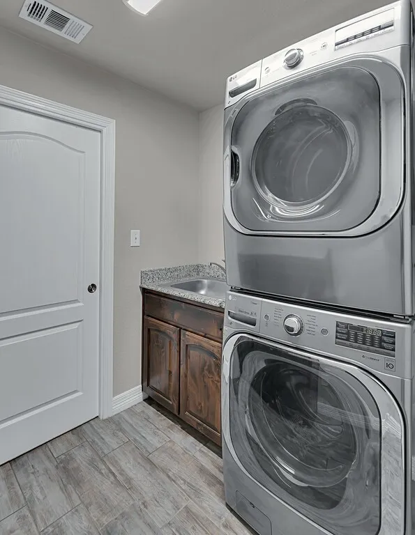 Wood-finish tile flooring, a utility sink with granite-style countertop, and dark wood cabinetry