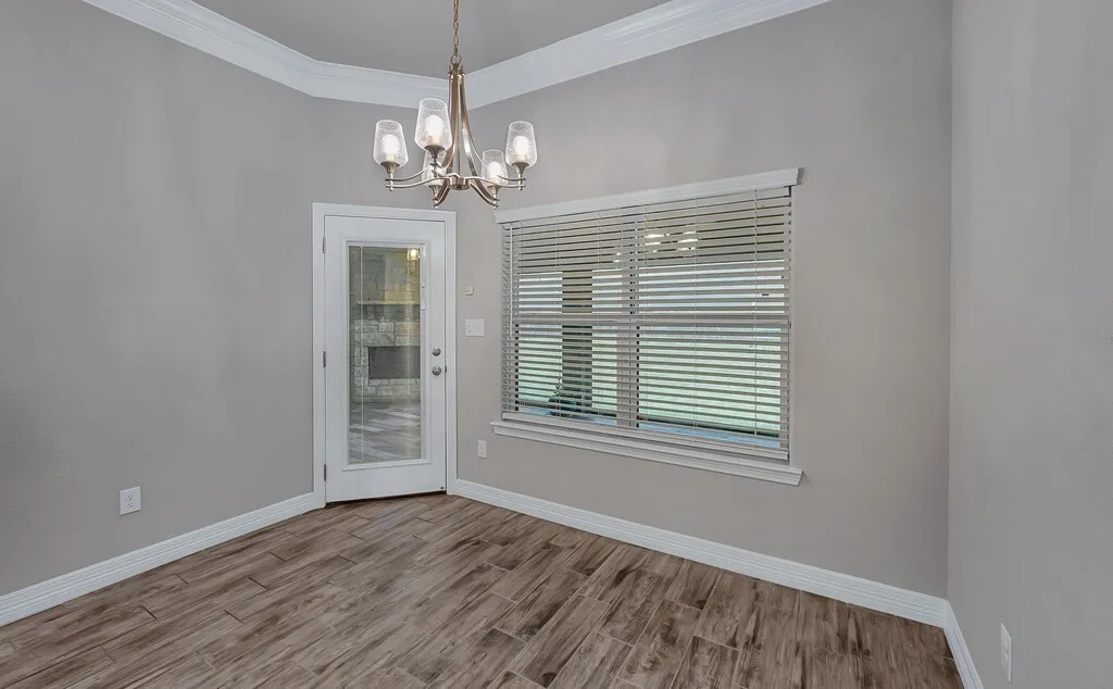 Wood-finish tile flooring, crown molding, a modern chandelier, a glass-paned door, and a large window with blinds