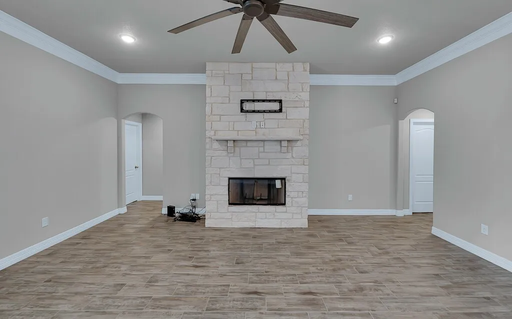 Stone fireplace with a hearth, wood-finish flooring, ceiling fan, recessed lighting, and arched doorways