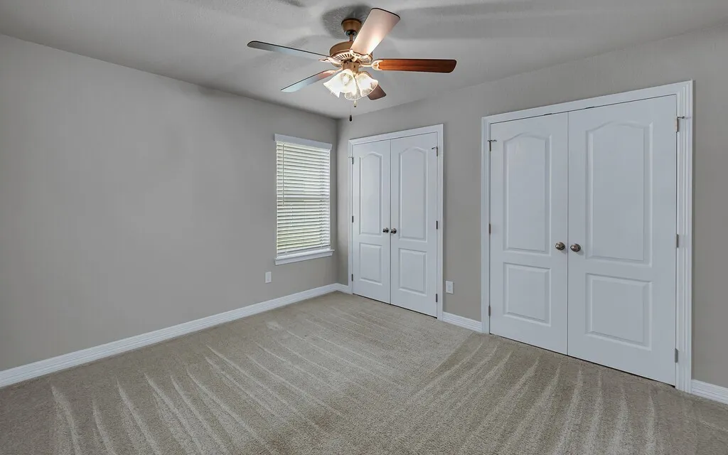 Neutral wall color, wall-to-wall carpeting, ceiling fan with integrated lighting, and two sets of double-door closets