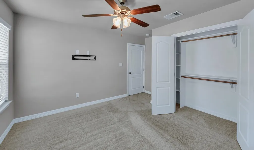 Plush carpeting, ceiling fan with integrated lighting, window with blinds, and a built-in closet with shelving and hanging rods