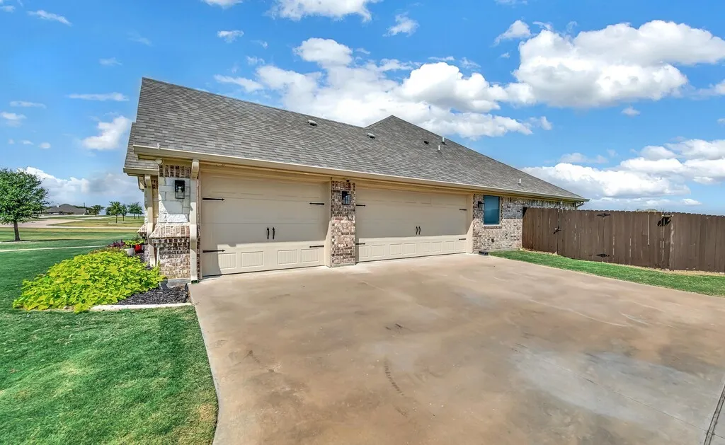 Three-car garage with panel doors, stone and brick facade, concrete driveway, and wood fence