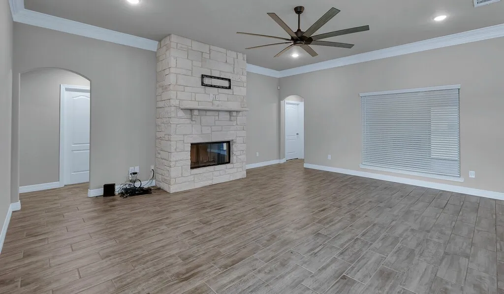 Spacious interior featuring wood-finish flooring, a stone-clad fireplace, and a ceiling fan with integrated lighting