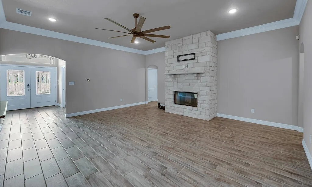 Stone fireplace with a mantle, wood-finish flooring, ceiling fan, recessed lighting, and crown molding