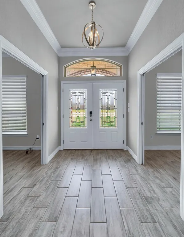 Double front entry doors with decorative glass inserts, an arched transom window, wood-finish flooring, and a contemporary ceiling light fixture