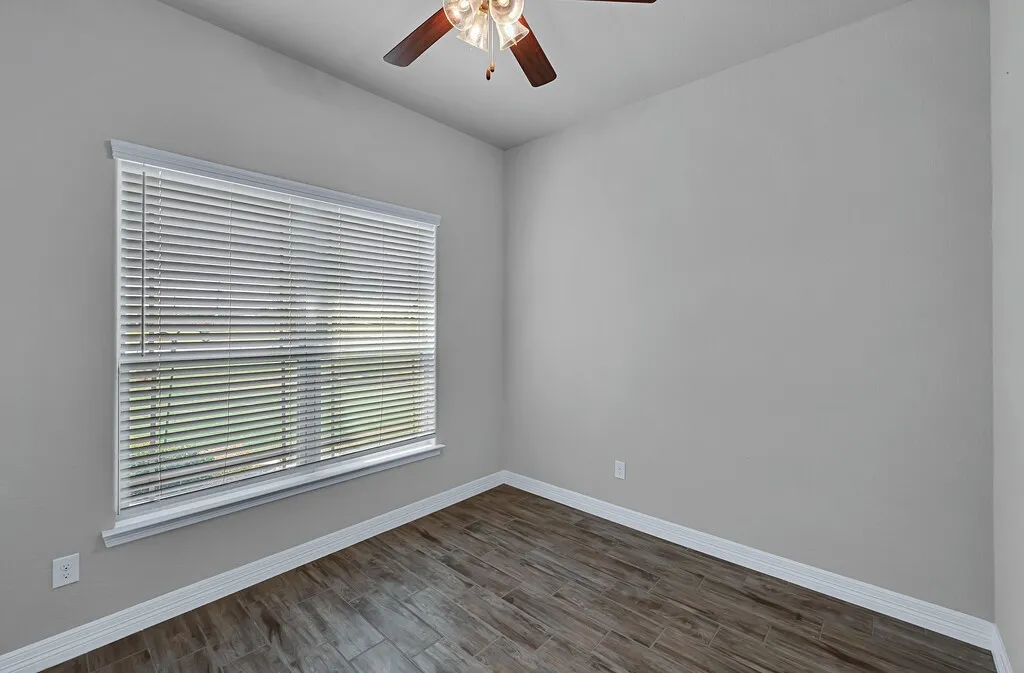 Neutral wall color, wood-finish flooring, ceiling fan with light fixture, window with horizontal blinds, white trim