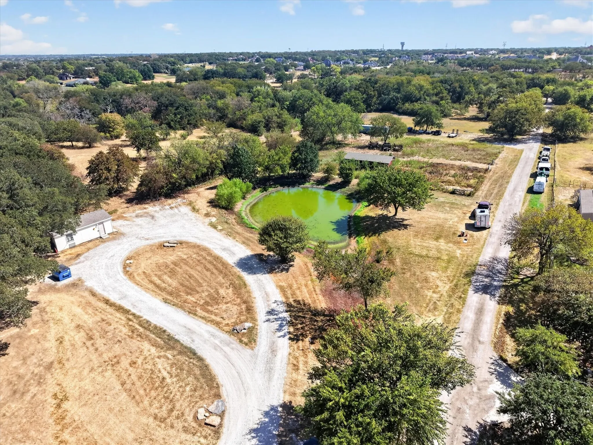 Expansive aerial view showcasing the property, open acreage, mature trees, pond, and surrounding landscape.