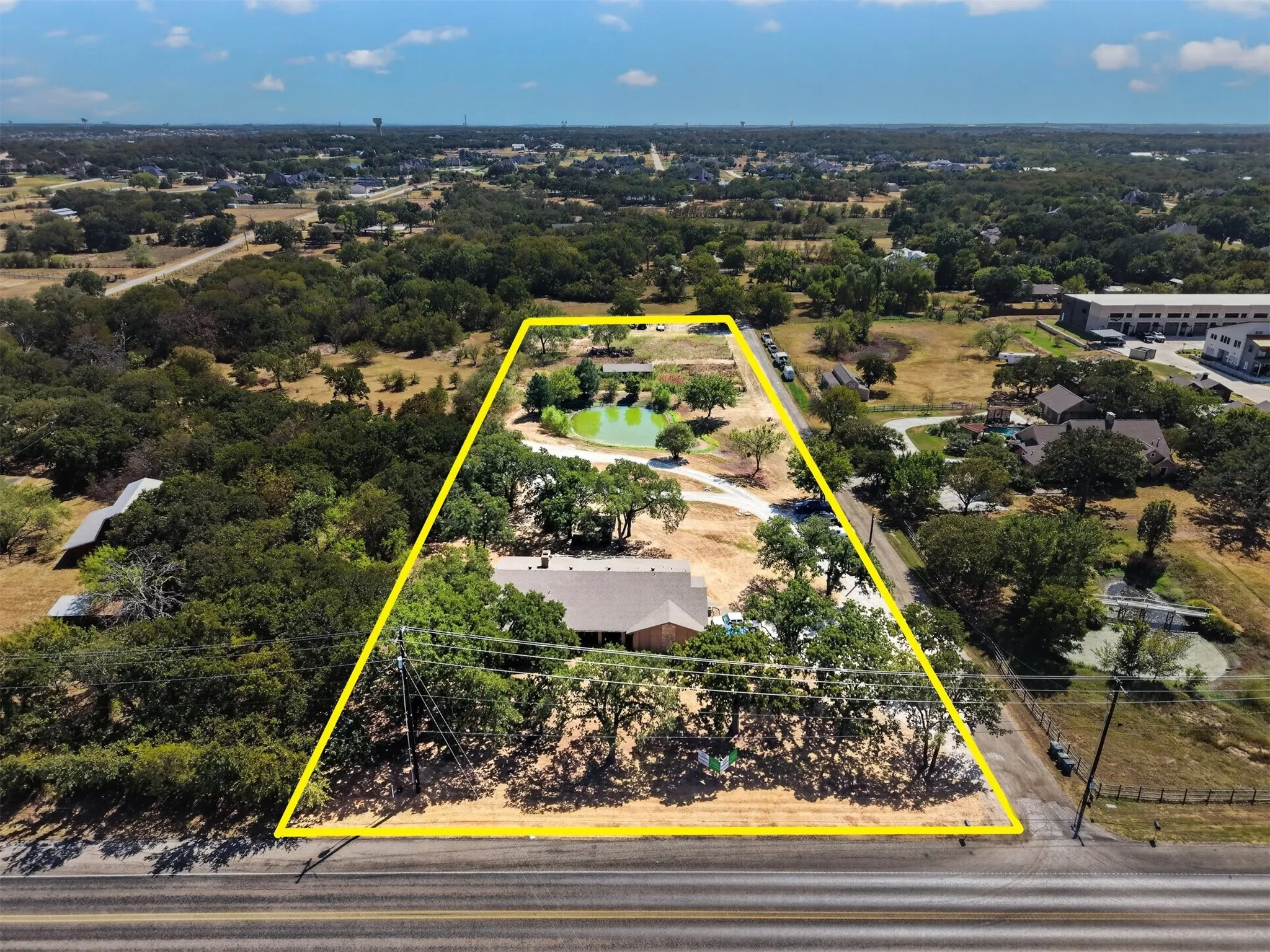 FM 407 frontage with property boundaries outlined, showing the existing residence, mature tree coverage, pond, and generous acreage beyond.