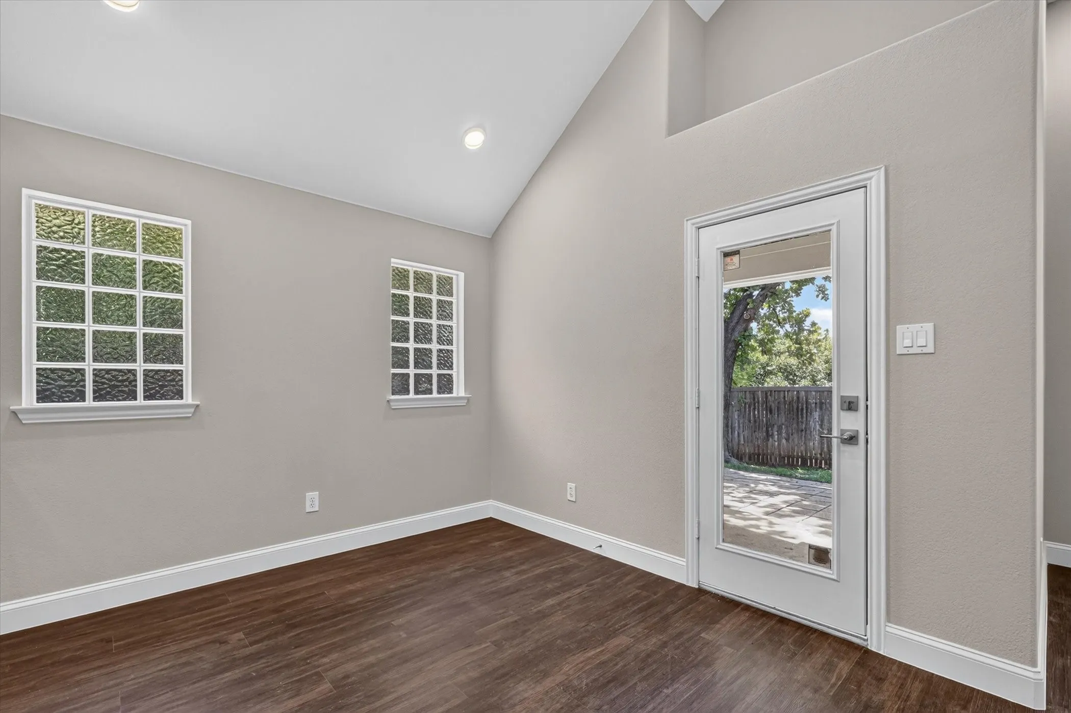 Vaulted ceiling with recessed lighting, wood-finish flooring, white trim, and a glass-paneled door