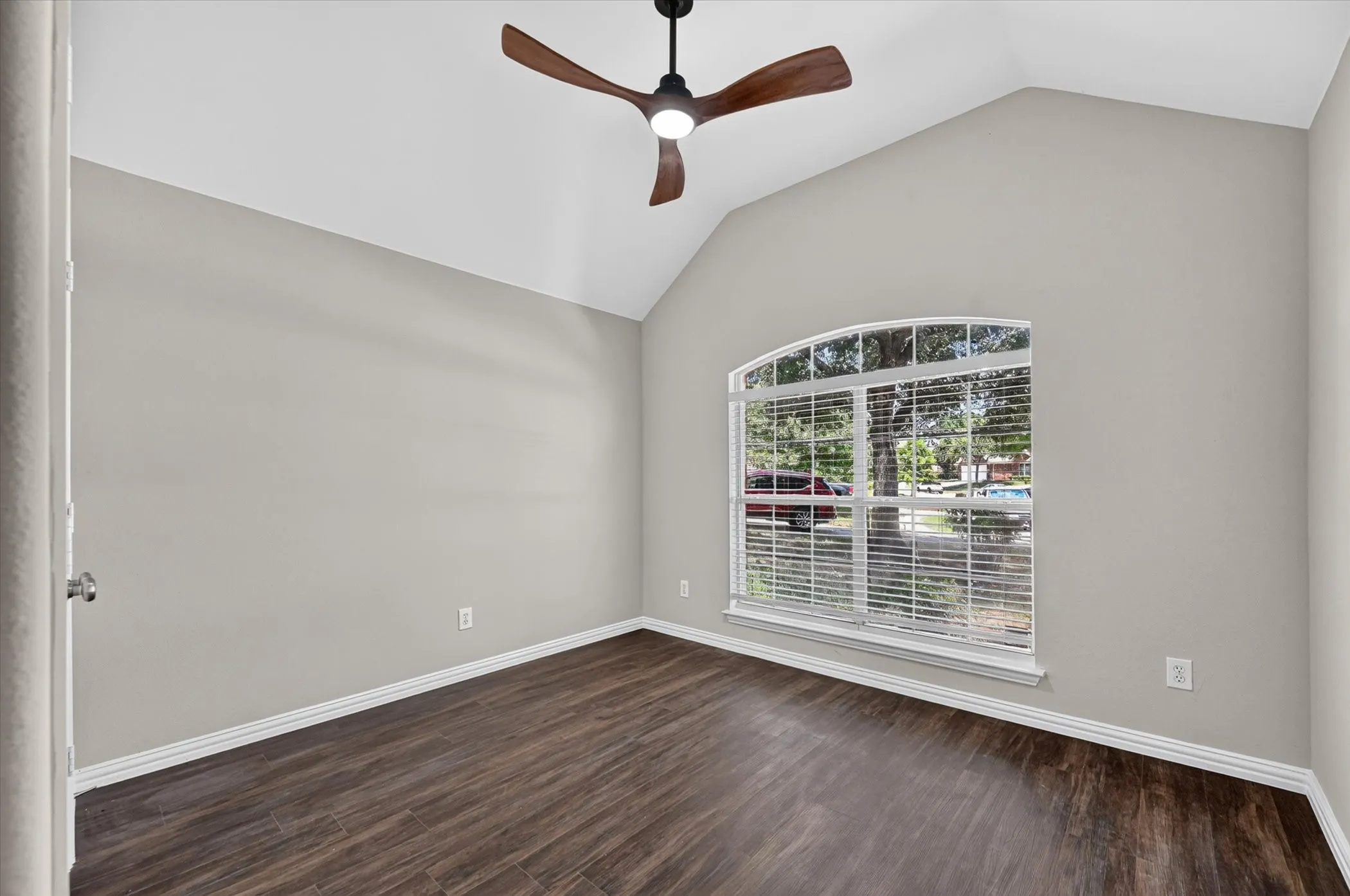 Vaulted ceiling with a ceiling fan, wood-finish flooring, and an arched window with blinds