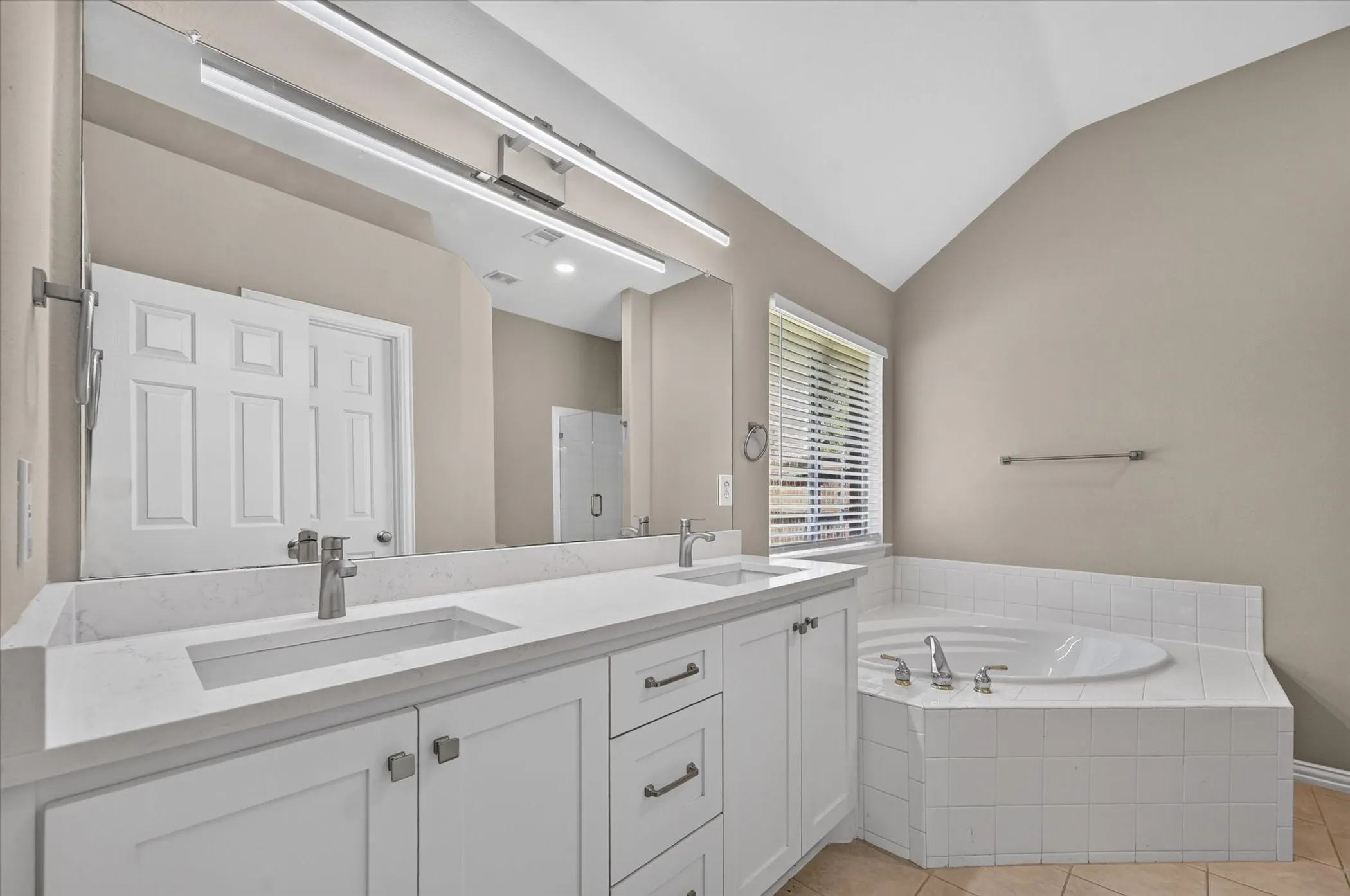 Dual vanity with integrated sinks and white cabinetry, recessed lighting, large soaking tub with tiled surround, and vaulted ceiling