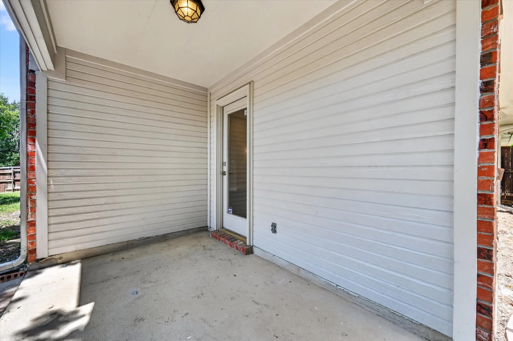 Covered patio featuring concrete flooring, horizontal siding, brick accents, and an exterior light fixture