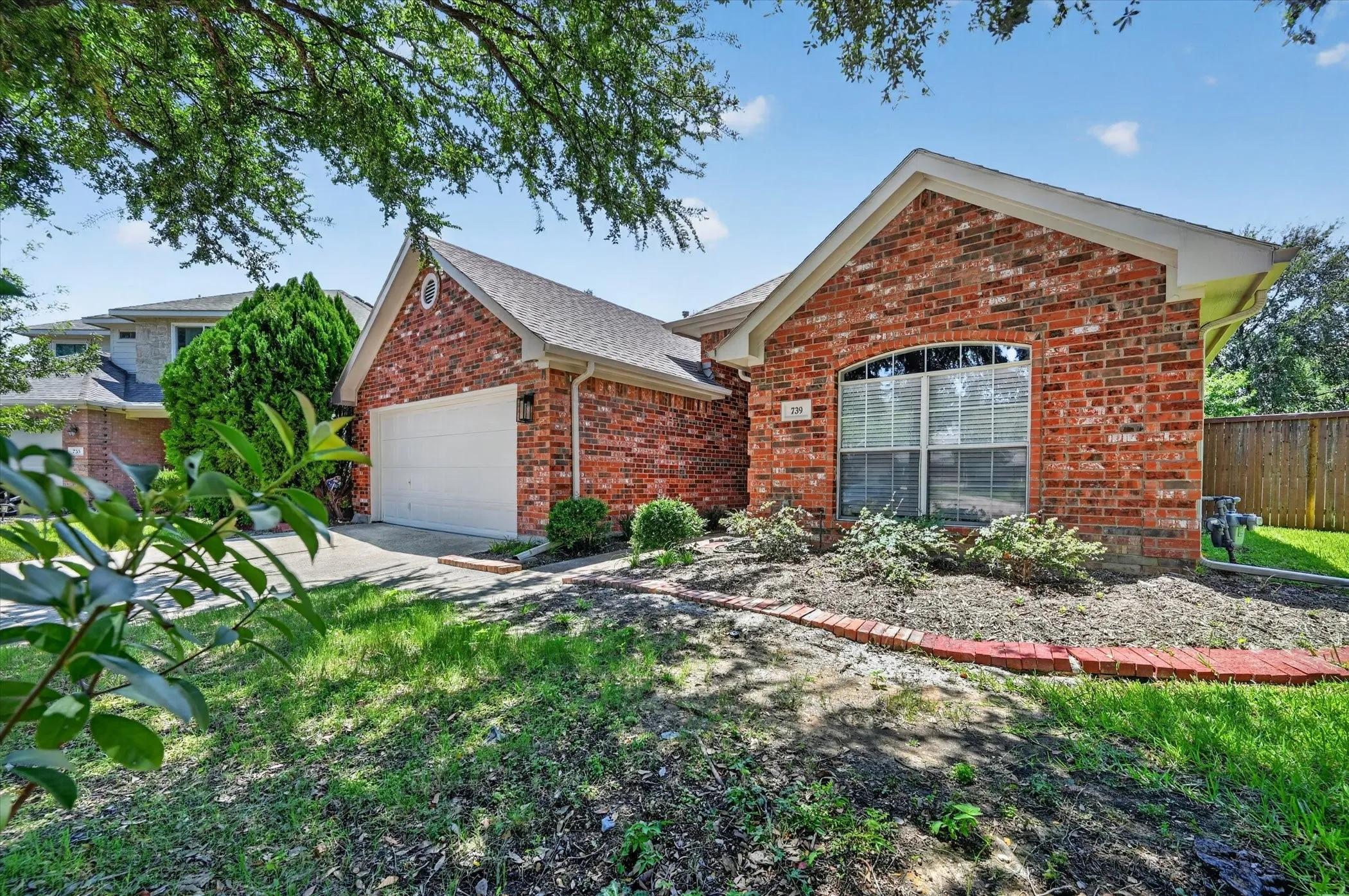 Red brick exterior with white trim, arched window, attached garage, and landscaped front garden bed