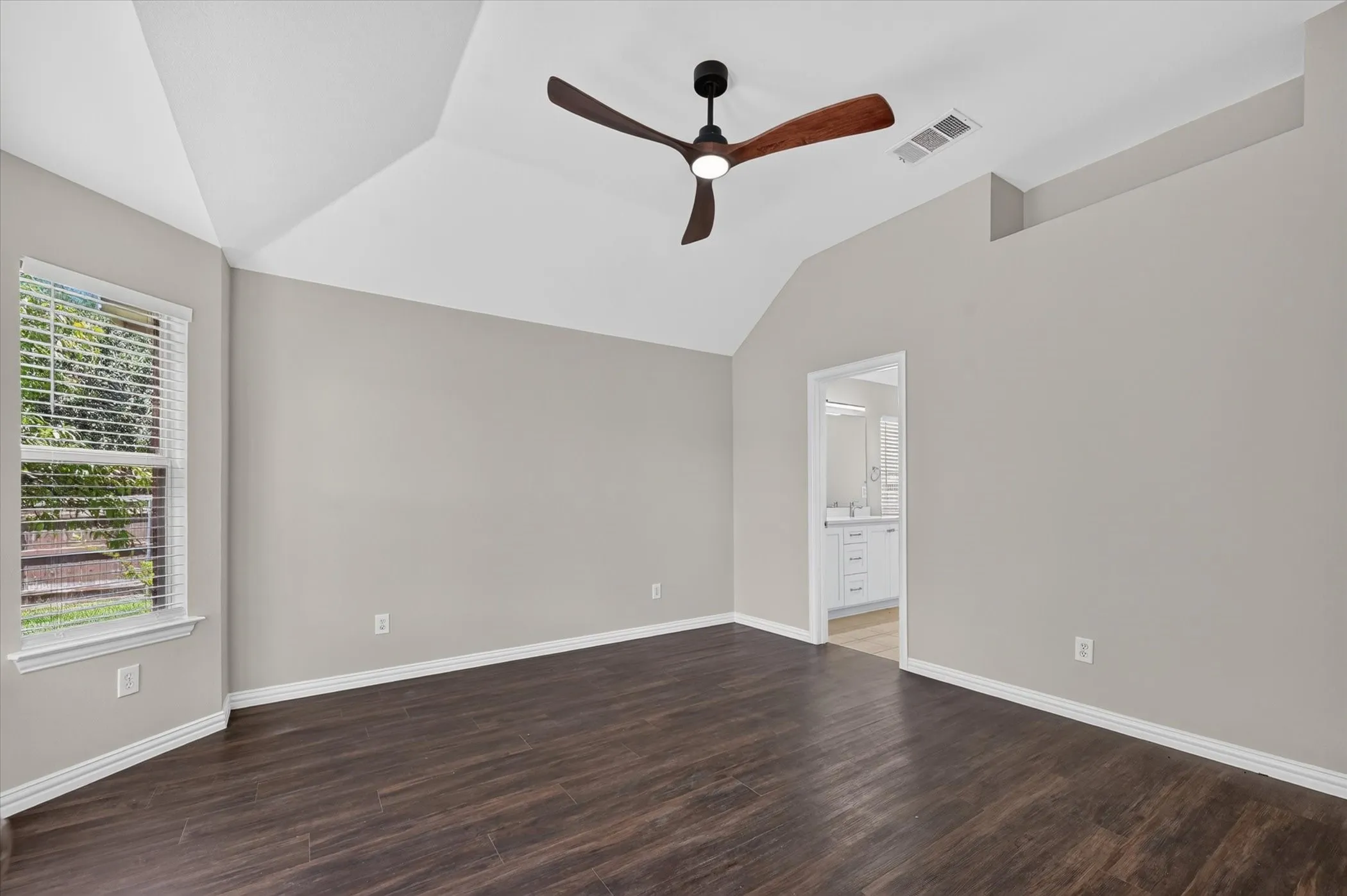 Vaulted ceiling with a contemporary ceiling fan, wood-finish flooring, and a large window with blinds