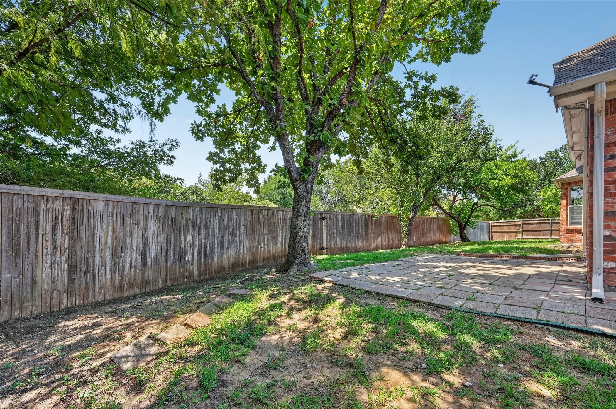 Expansive backyard featuring a mature shade tree, a wood privacy fence, and a paver patio