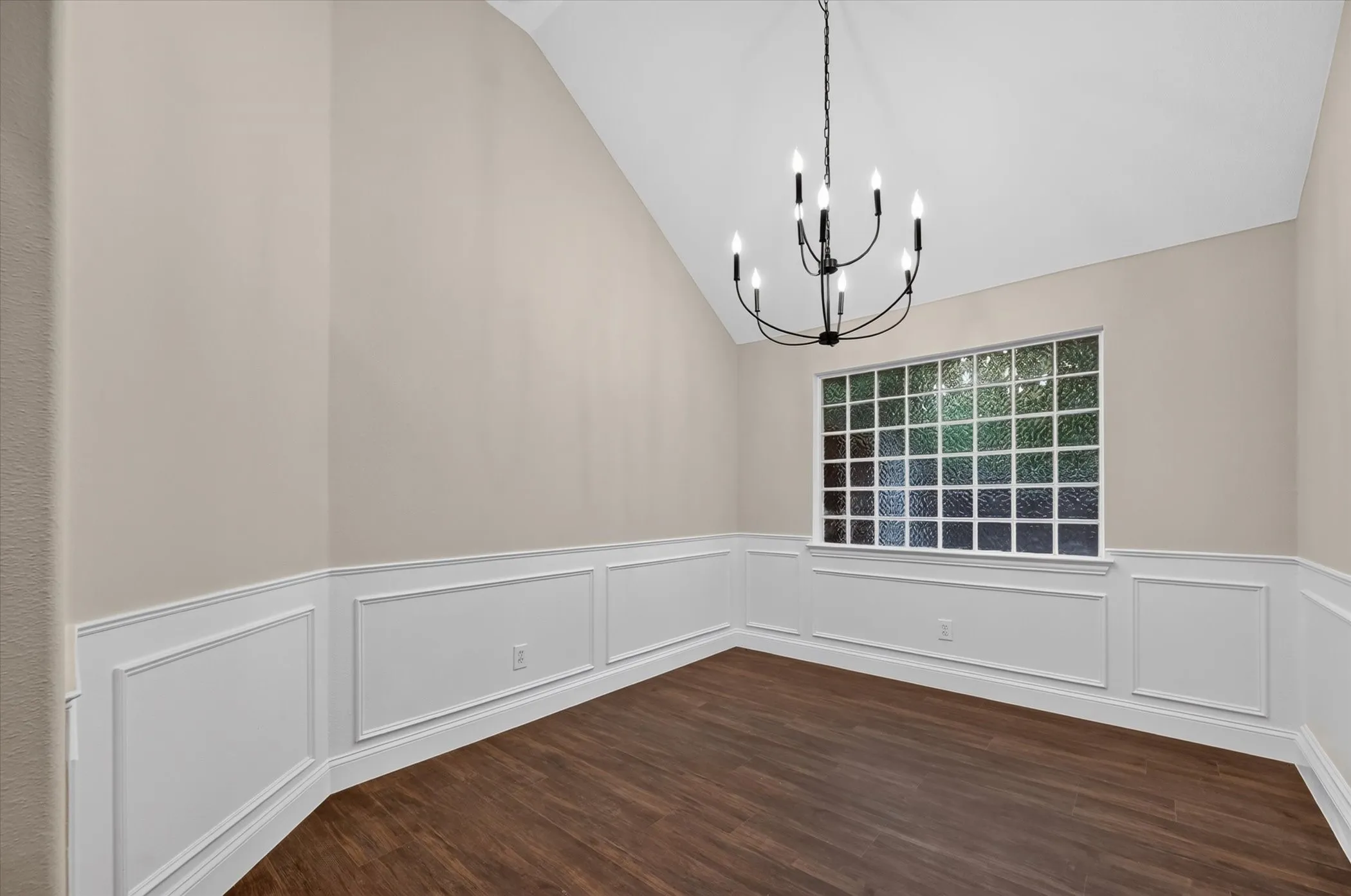 Vaulted ceiling with an iron chandelier, wood-finish flooring, and wainscoting with decorative molding