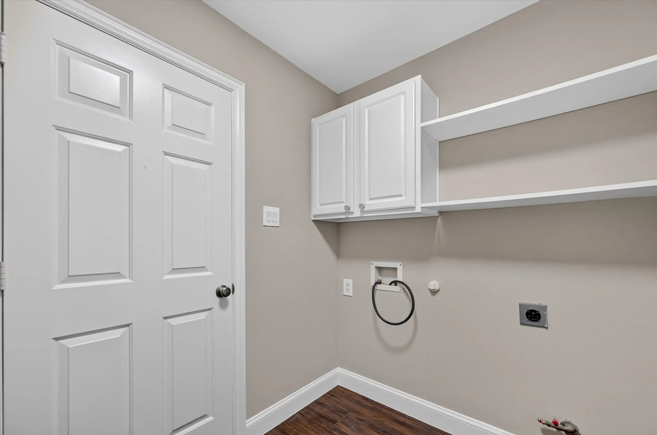 Utility area featuring wood-finish flooring, white paneled door, wall-mounted cabinetry, and open shelving