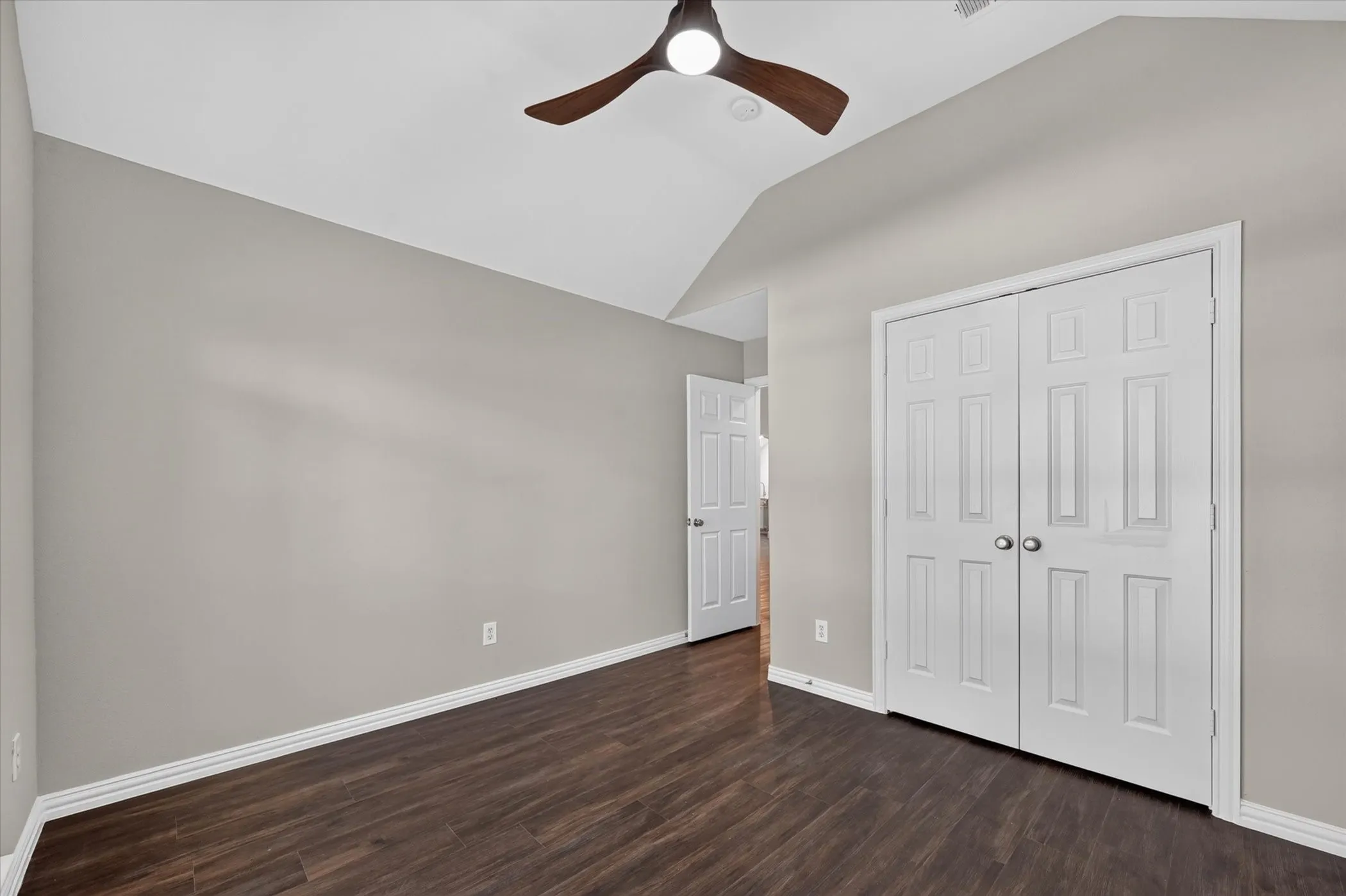 Vaulted ceiling with a ceiling fan, wood-finish flooring, light gray wall paint, and bi-fold closet doors