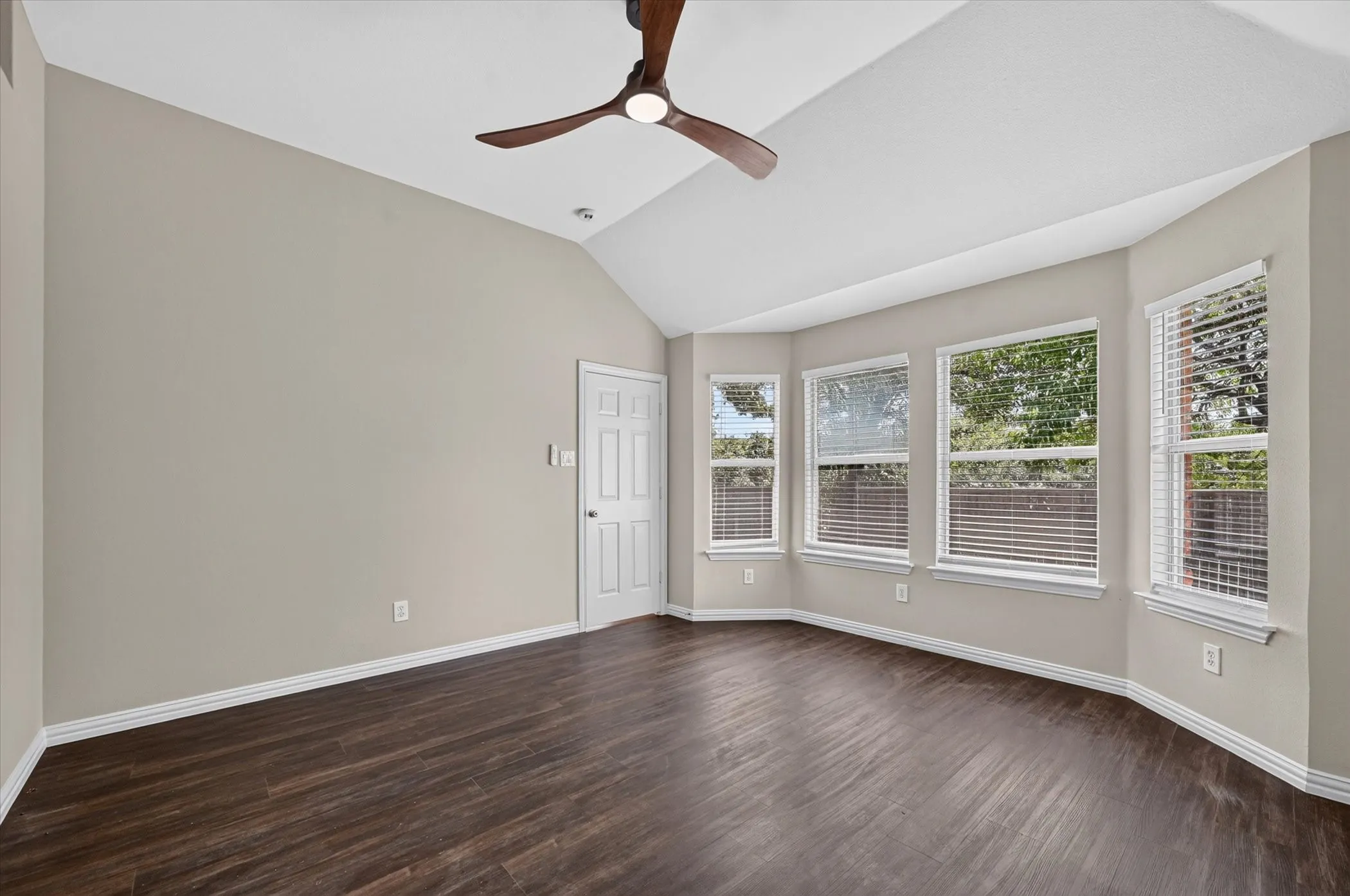 Vaulted ceiling with a wood-finish ceiling fan, dark wood-finish flooring, and multiple windows with blinds