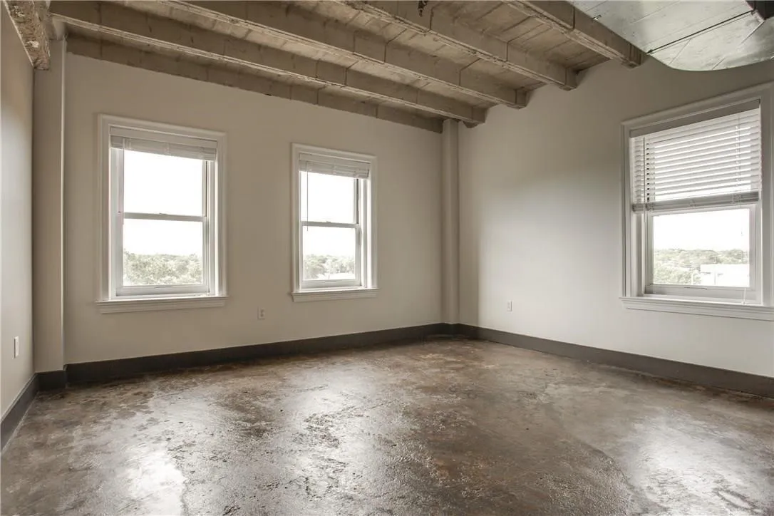 Exposed ceiling joists with concrete flooring, multiple windows, and a neutral wall color