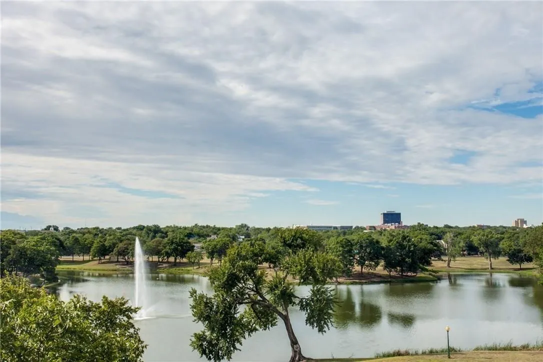 Scenic lake with a prominent water fountain, surrounded by mature trees, and distant urban structures