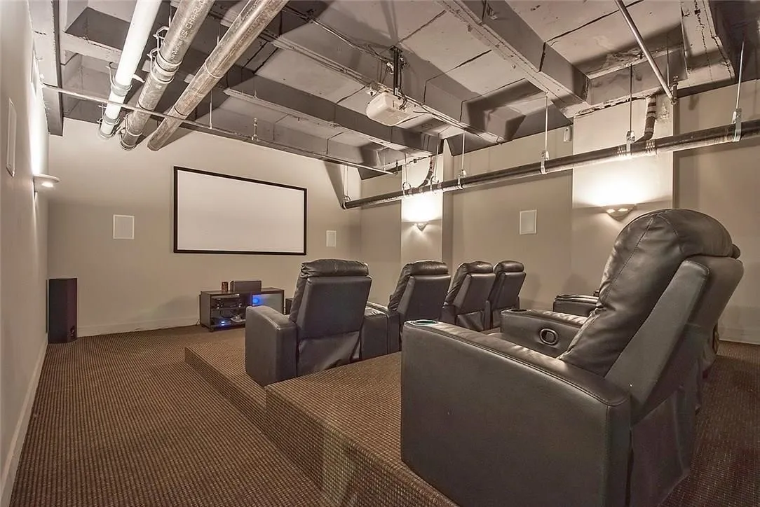 Media room featuring a projector, wall-mounted screen, elevated seating platform, and integrated wall sconces