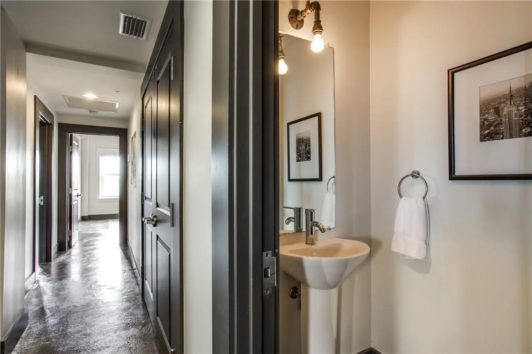 Pedestal sink with chrome fixtures, wall-mounted light fixture, and dark paneled doors