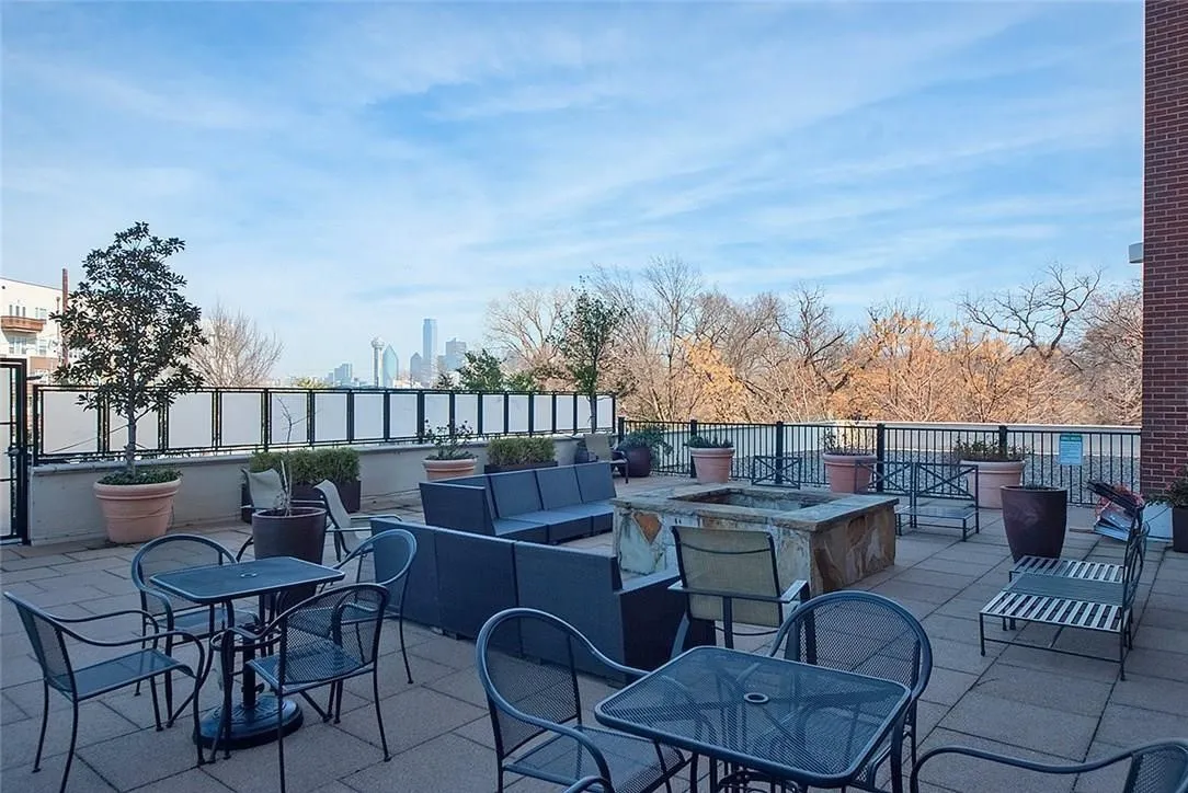 Paved outdoor terrace featuring a stone-clad fire pit, brick exterior wall, and a metal and frosted panel railing
