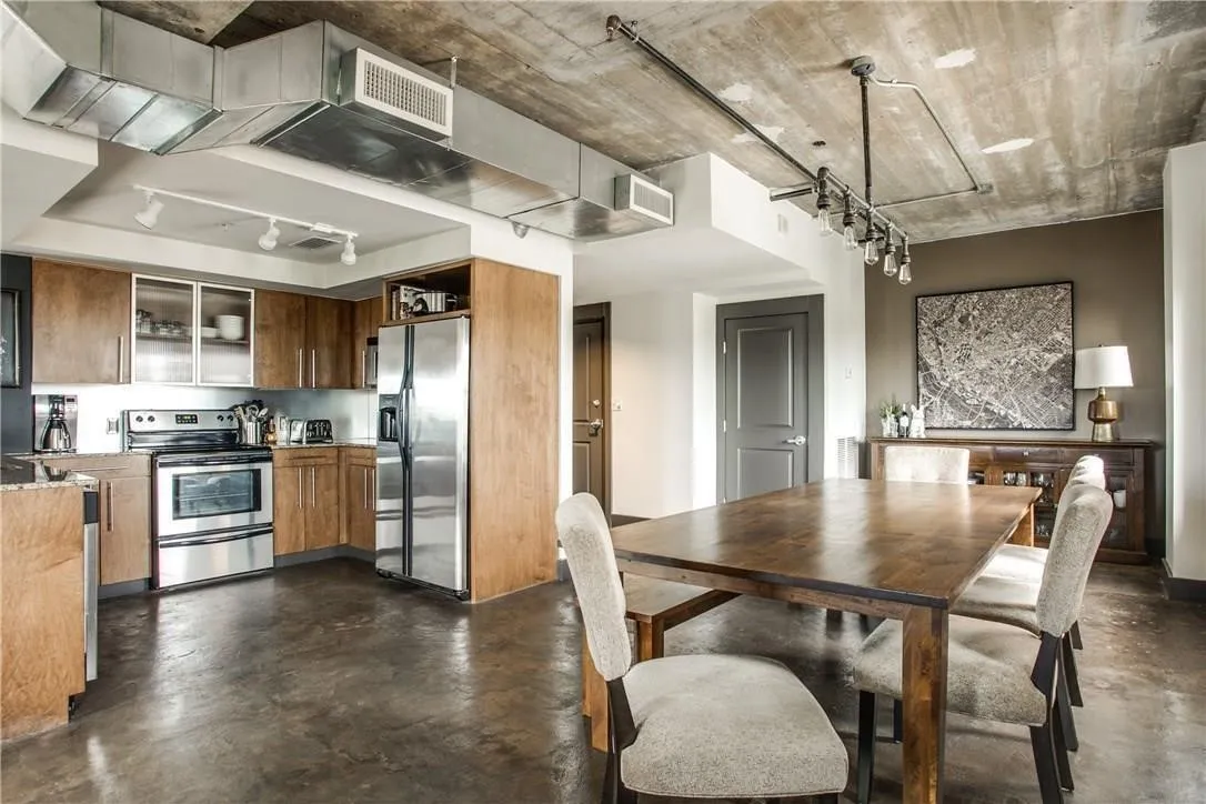 Exposed concrete ceiling with industrial ductwork, polished concrete flooring, stainless steel appliances, wood cabinetry, and track lighting
