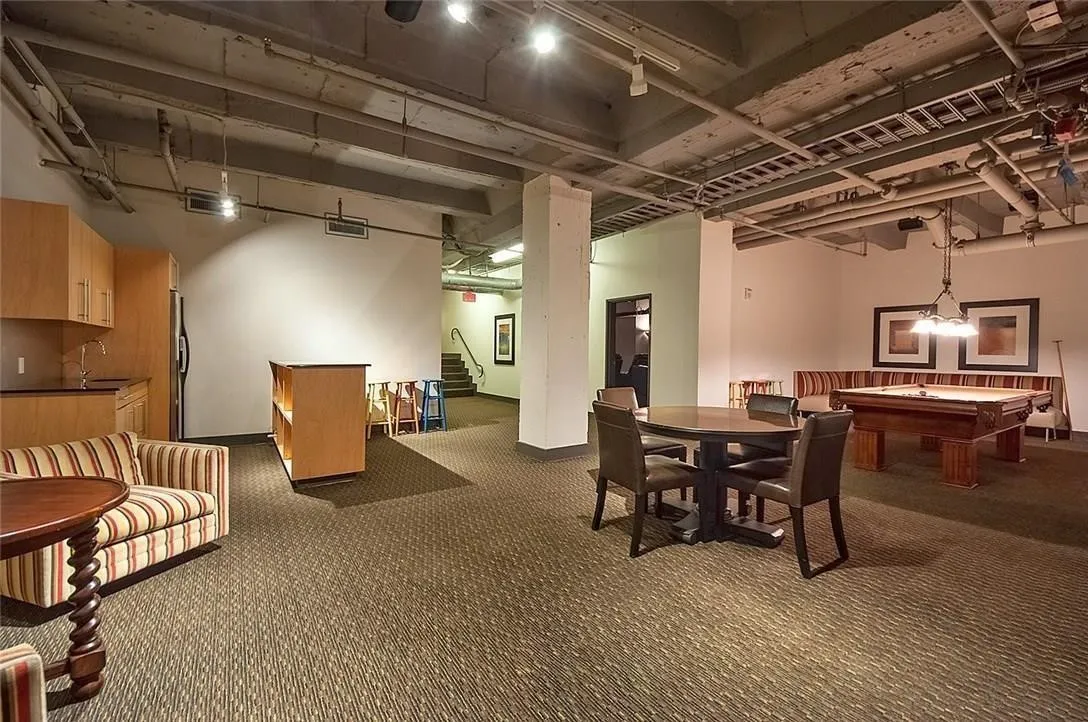 Open-concept common area featuring exposed ceiling elements, patterned carpet flooring, a built-in kitchen area with cabinetry, and a billiards table