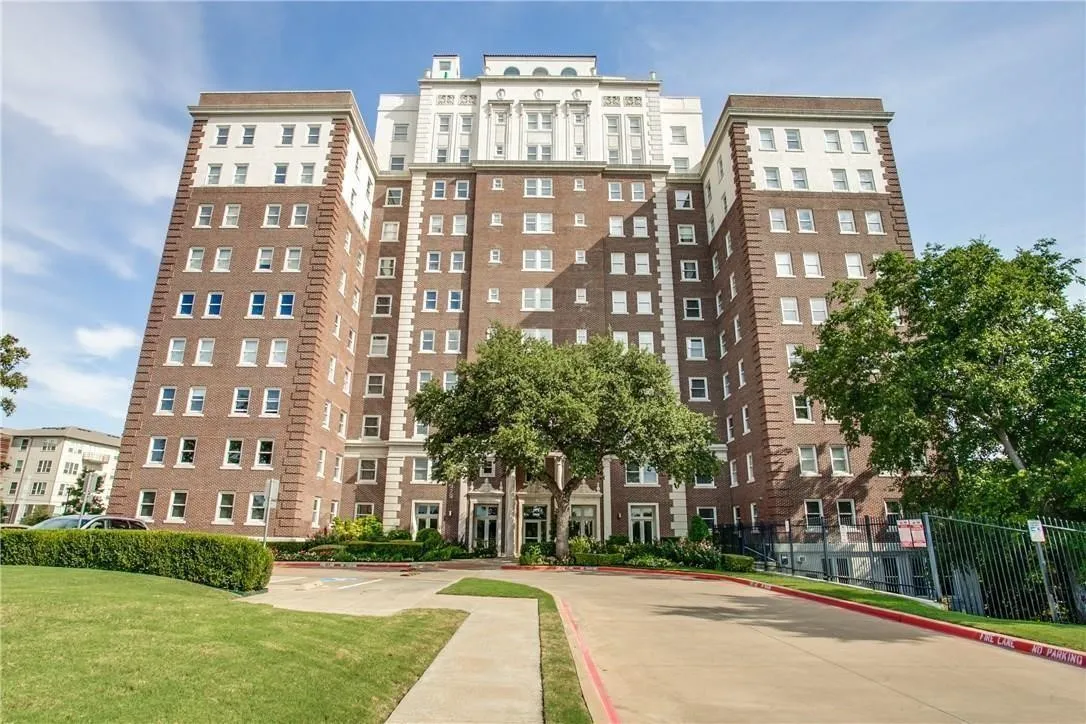 Multi-story brick building with white architectural detailing, featuring a structured entrance and a landscaped front lawn