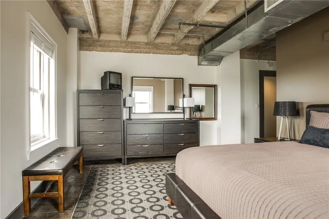 Concrete ceiling with exposed beams and ductwork, white window trim, and dark wood-finish flooring