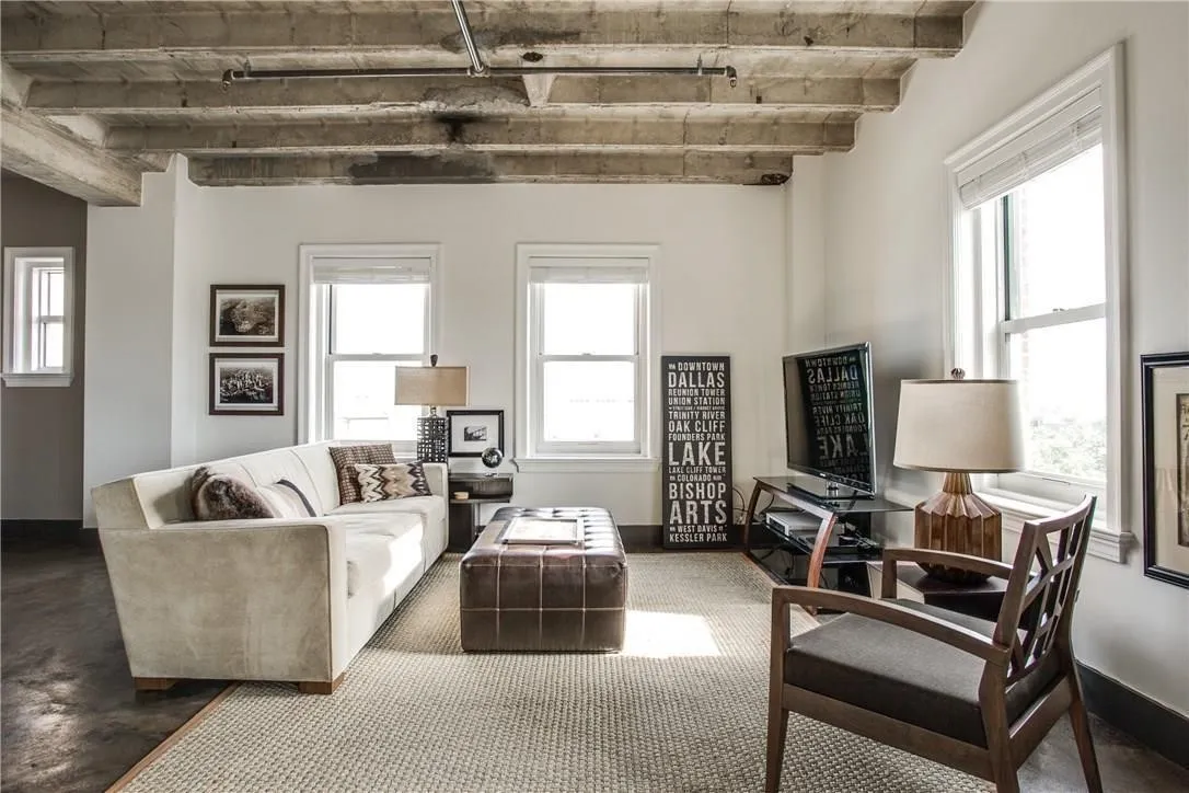 Exposed concrete ceiling with visible beams, multiple windows with white trim, light-colored walls, and dark-finish flooring