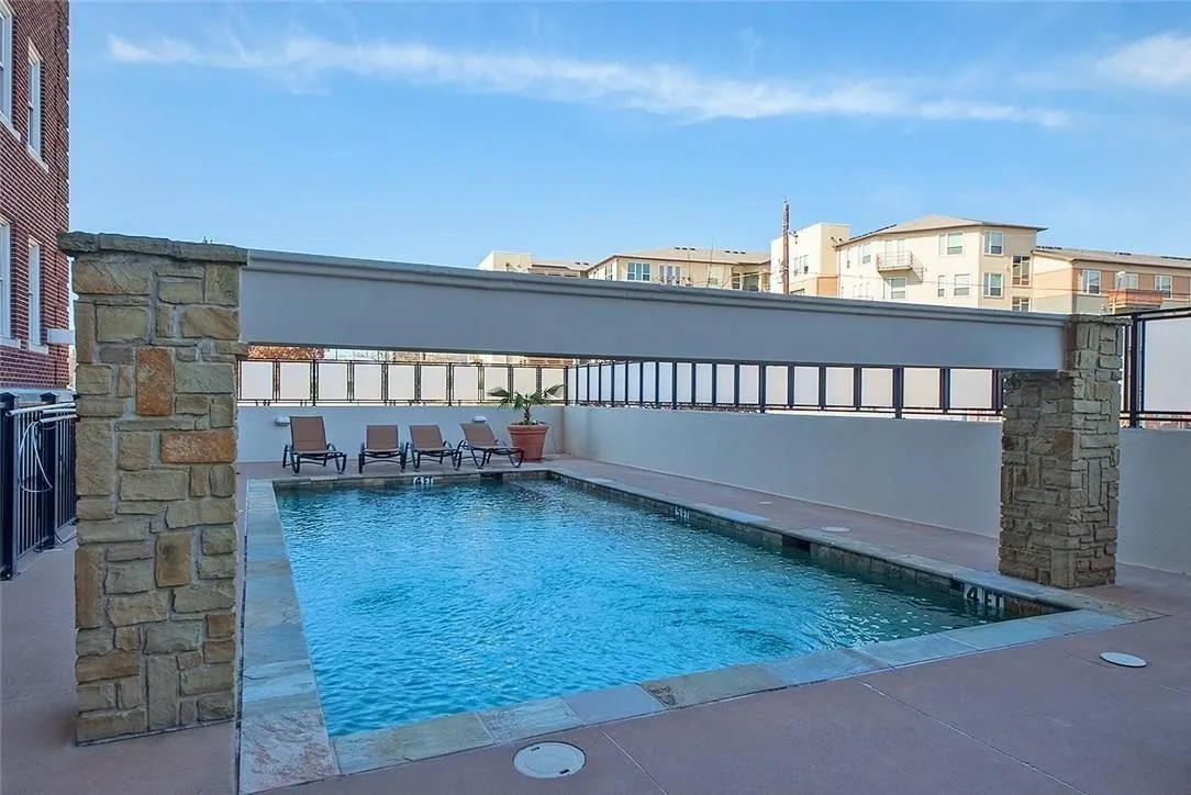 Outdoor swimming pool with concrete decking, stone-clad pillars, and a privacy wall