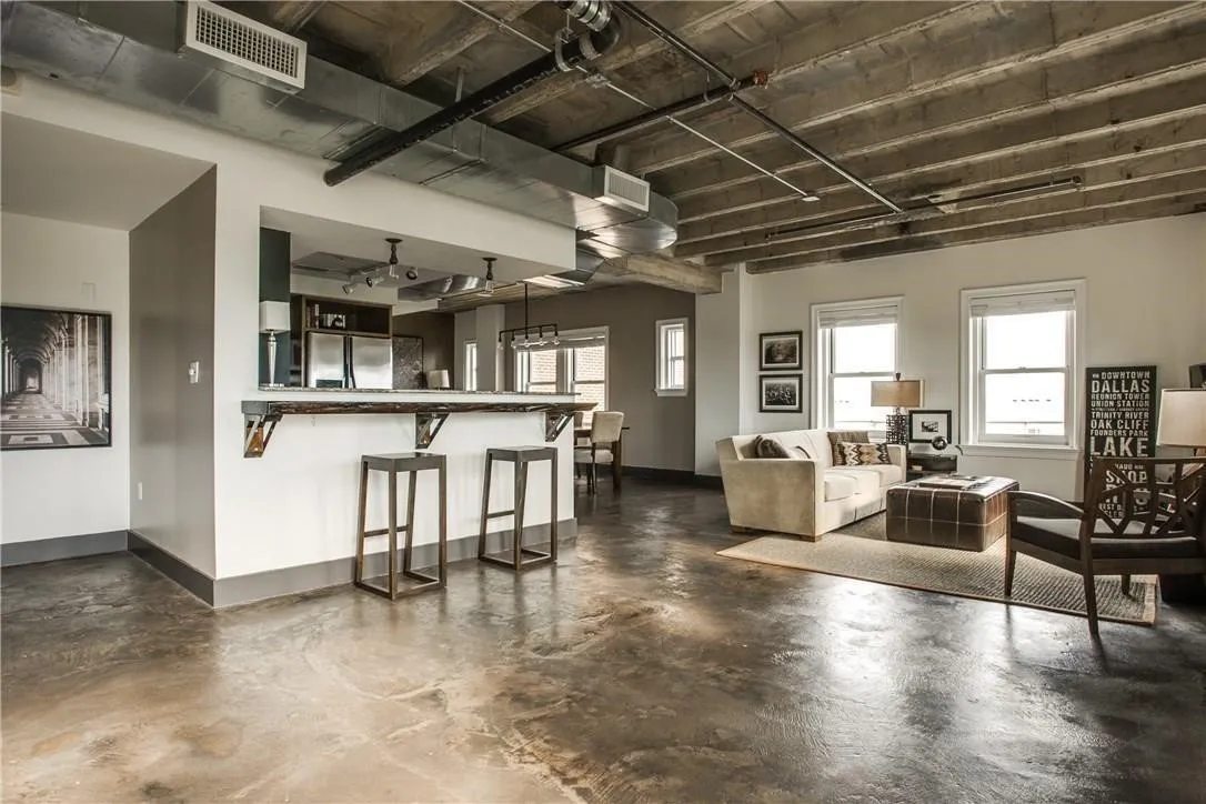 Polished concrete flooring, exposed concrete ceiling, industrial-style ductwork, kitchen pass-through with bar seating, and multiple windows