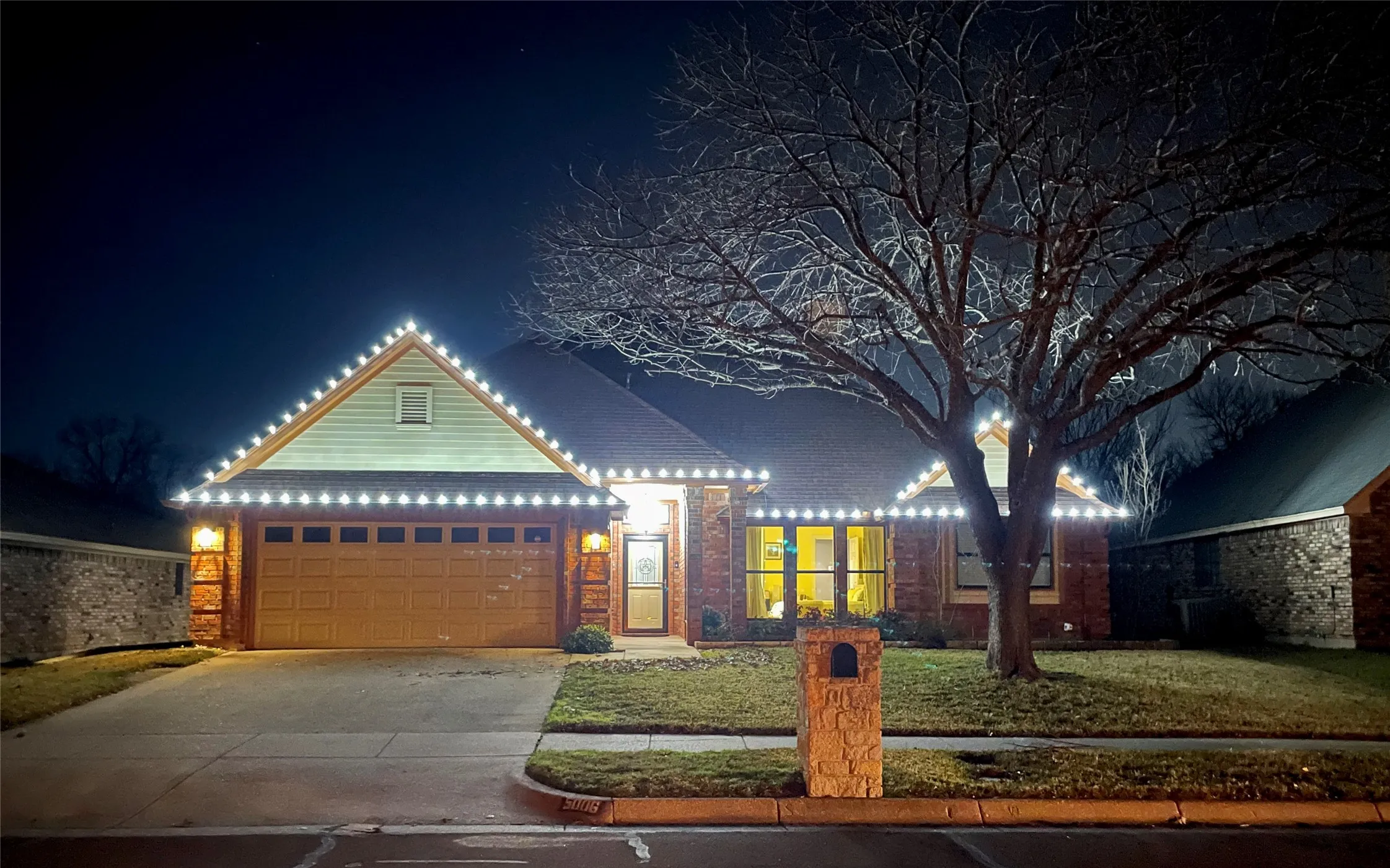 Brick and siding exterior with an attached two-car garage, mature front yard tree, and stone-clad mailbox