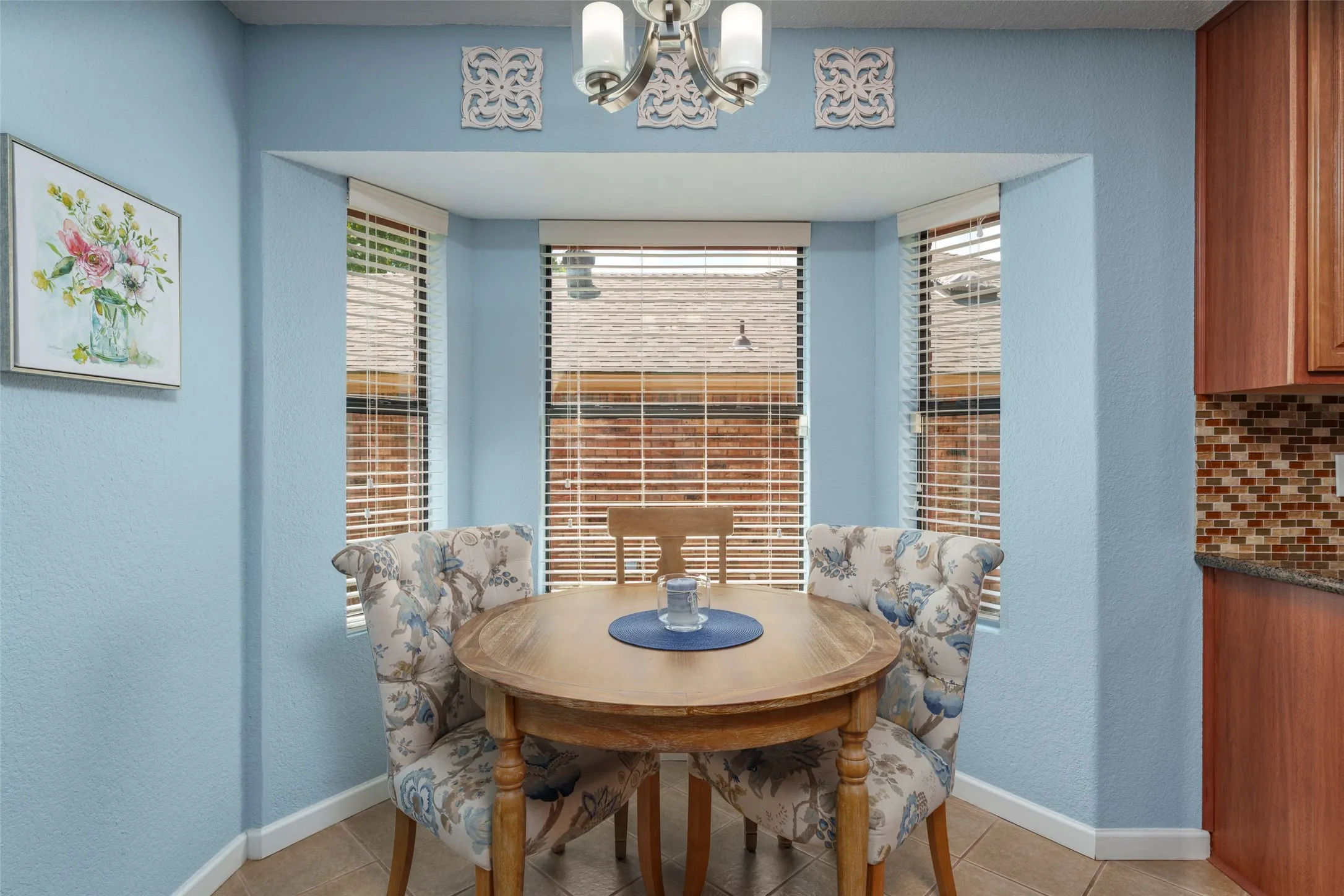 Bay window with blinds, tile flooring, wood-finish cabinetry, and mosaic tile backsplash