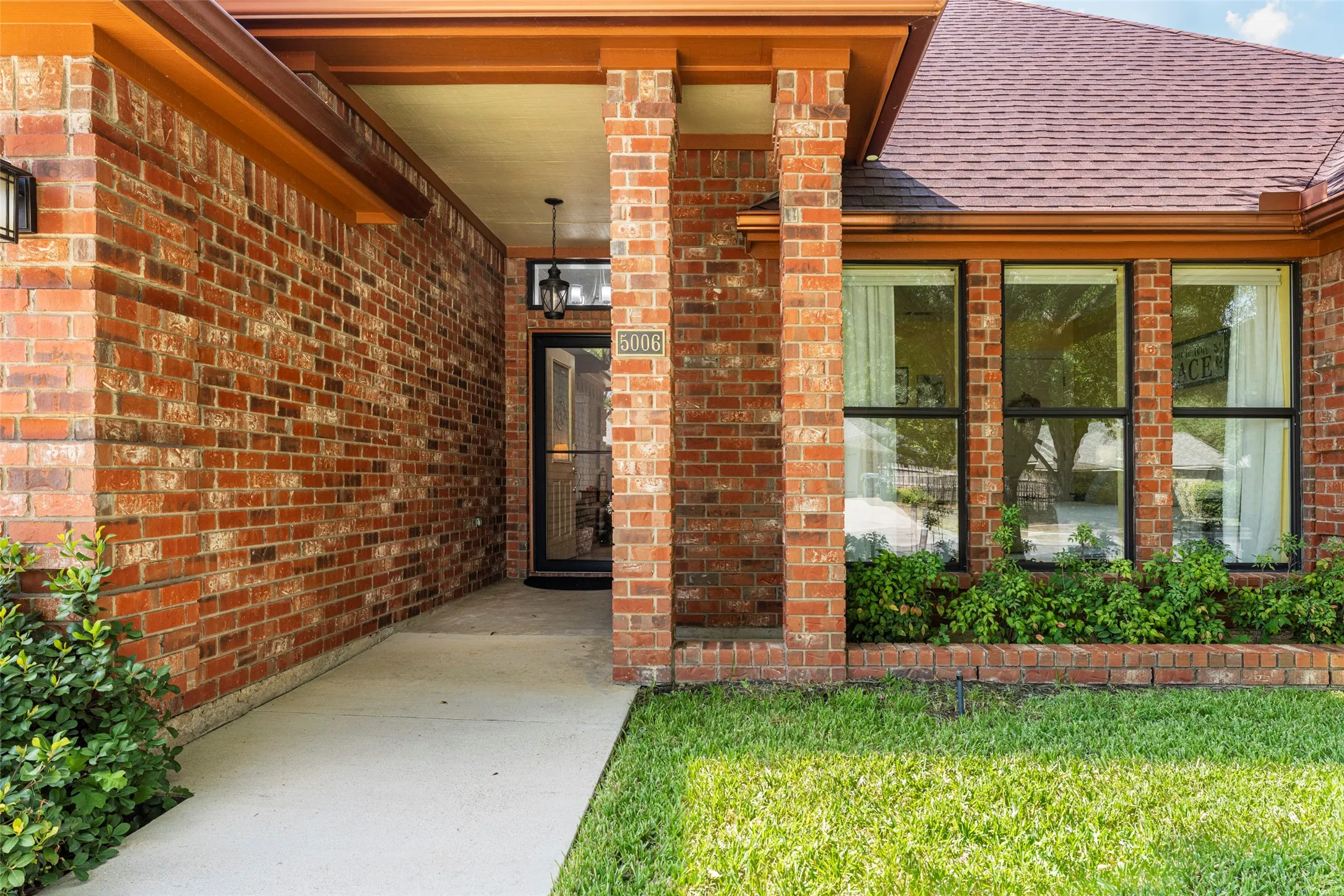Brick exterior facade with a covered entry, multiple windows, and exterior lighting