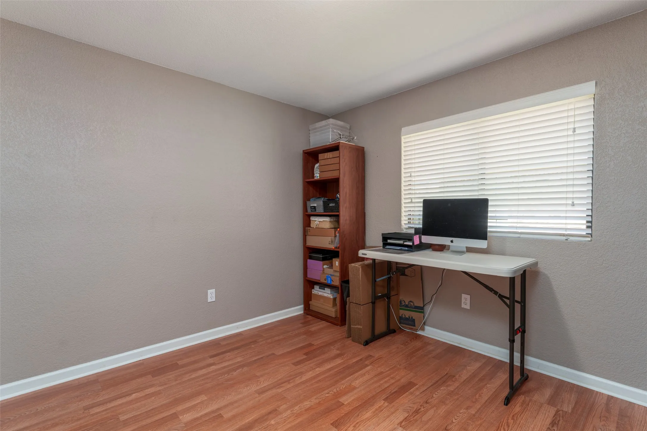 Wood-finish flooring, neutral wall color, and a window with horizontal blinds