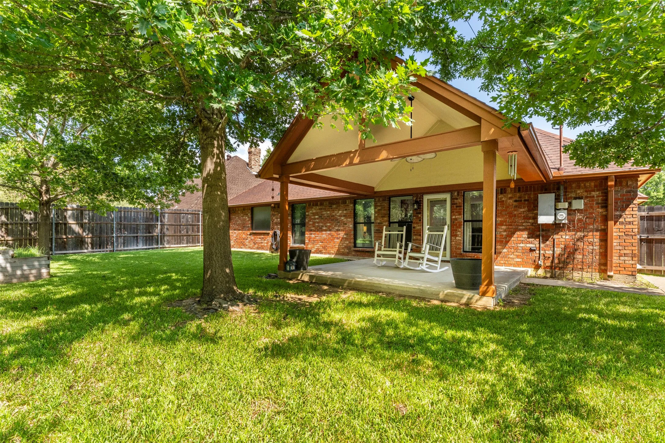 Expansive backyard featuring a manicured lawn, mature trees, and a covered patio with a vaulted ceiling. Small shed included