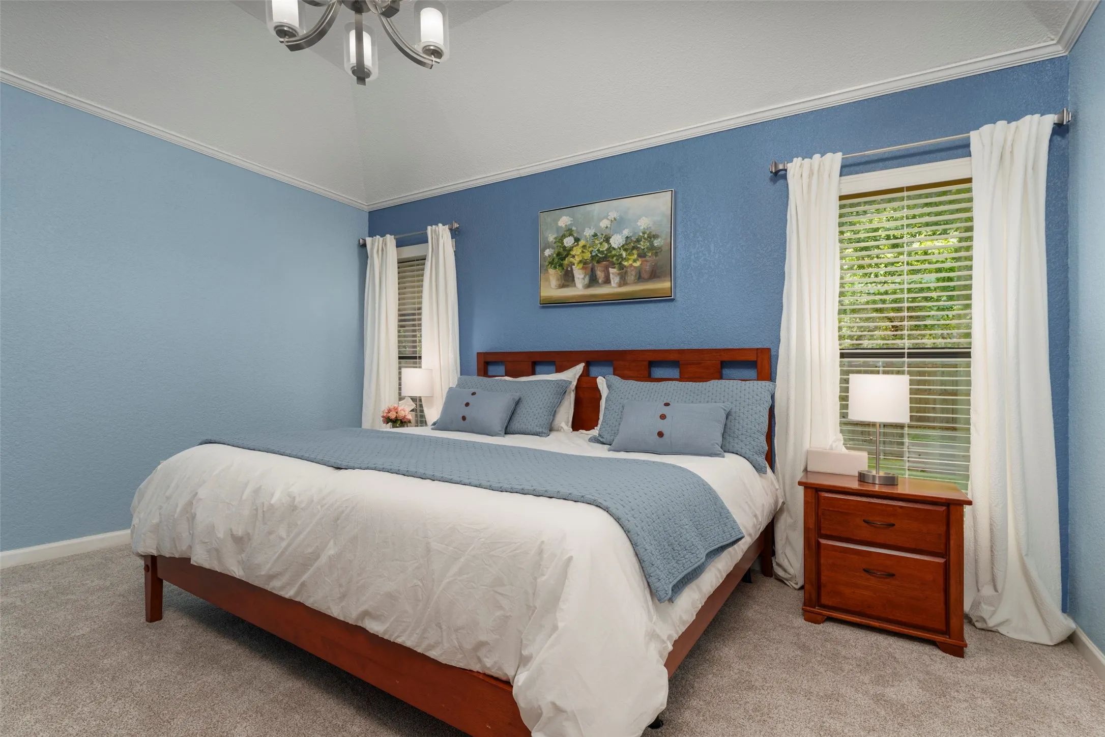 Vaulted ceiling with crown molding, textured walls, two large windows with blinds, and carpet flooring
