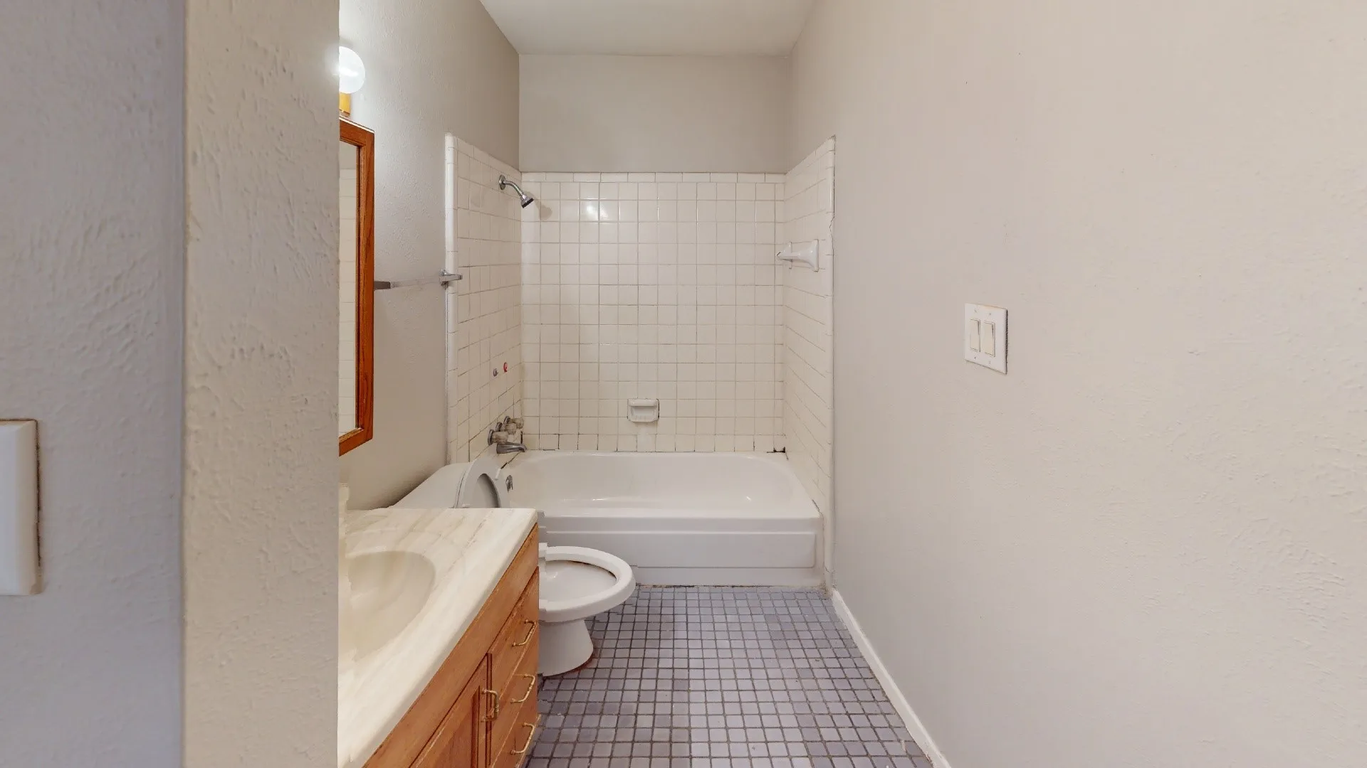 Bathroom featuring a full-size bathtub, white tile shower surround, wood-finish vanity with an integrated sink, and mosaic floor tiling