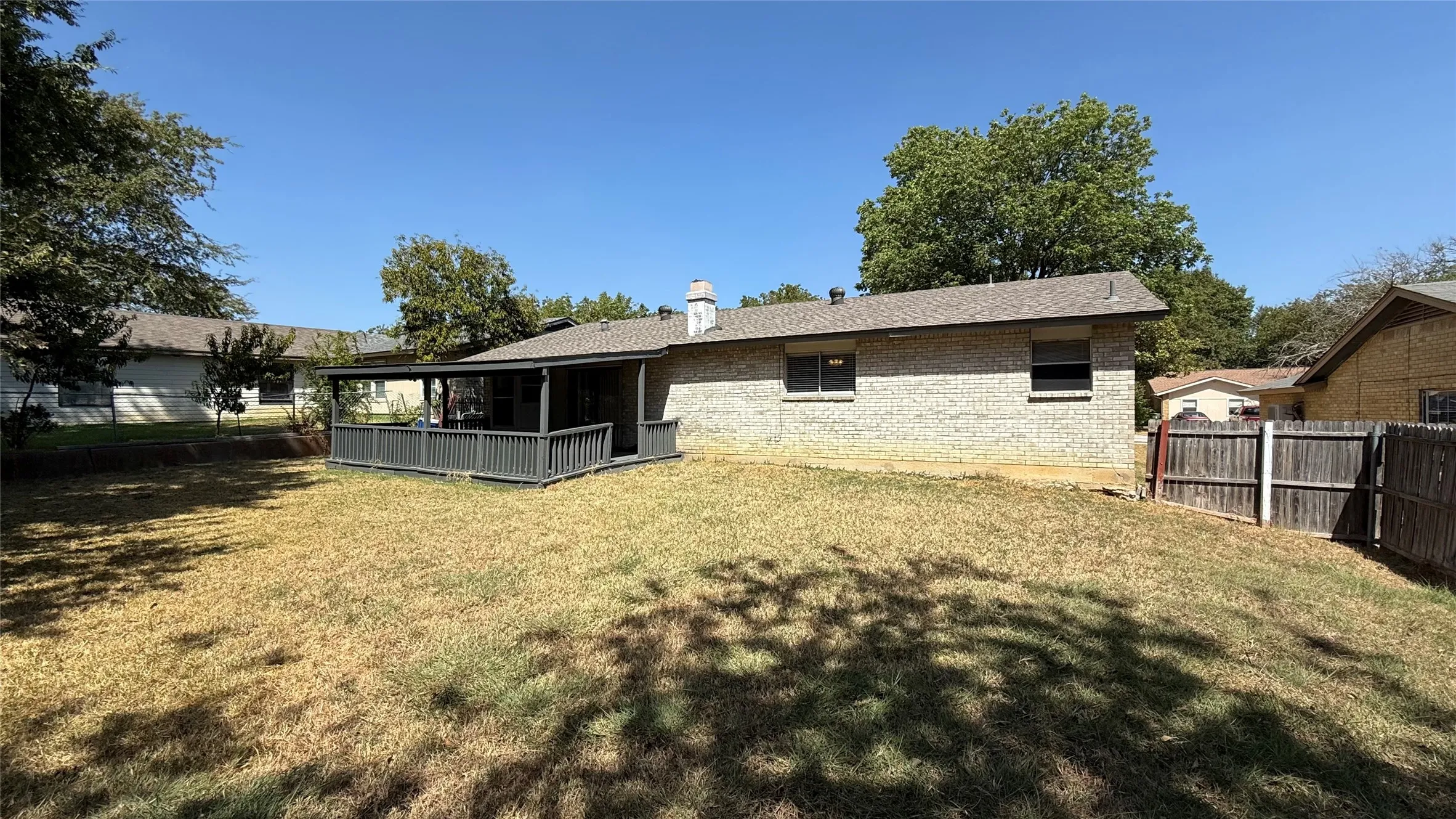 Expansive backyard featuring a covered patio with railing, light-colored brick exterior, and a wood privacy fence