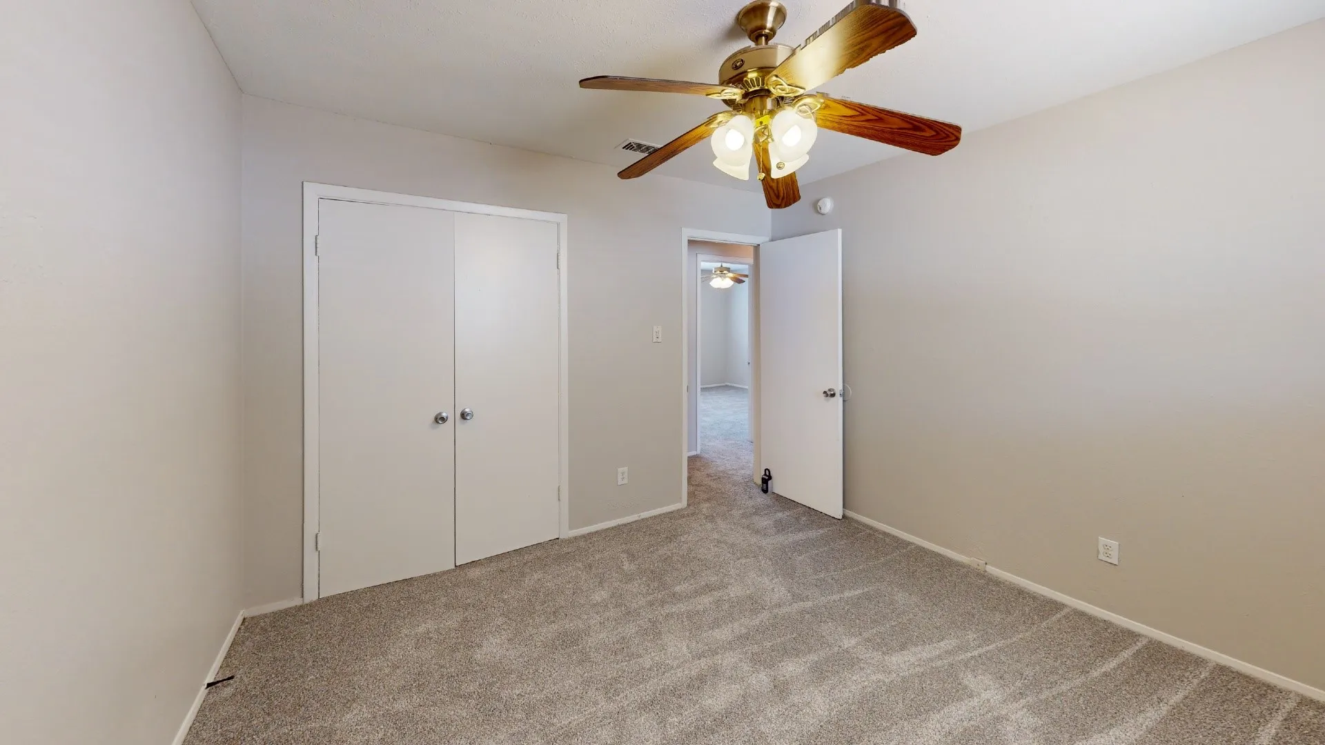 Neutral tone wall paint, textured carpet flooring, ceiling fan with integrated lighting, and white bi-fold closet doors