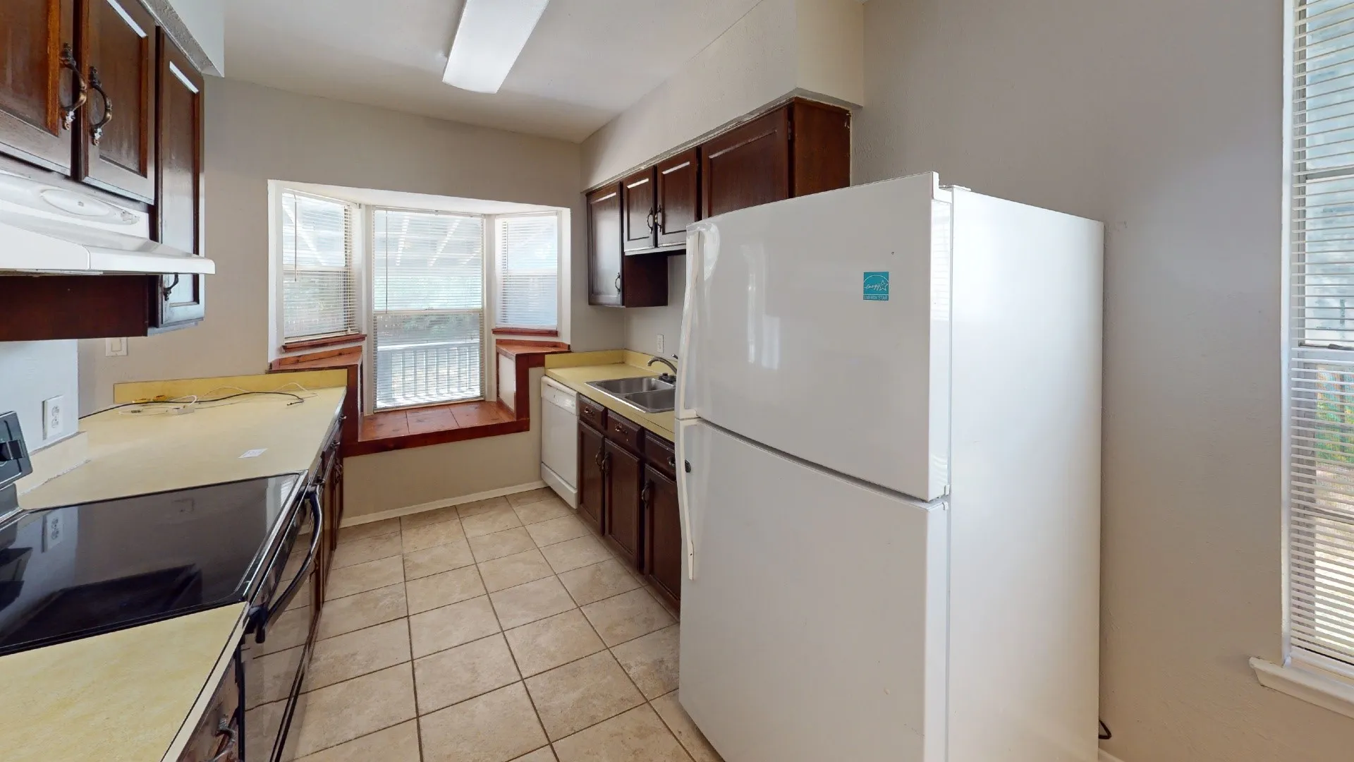 Kitchen featuring wood-finish cabinetry, tile flooring, a bay window, and a white refrigerator