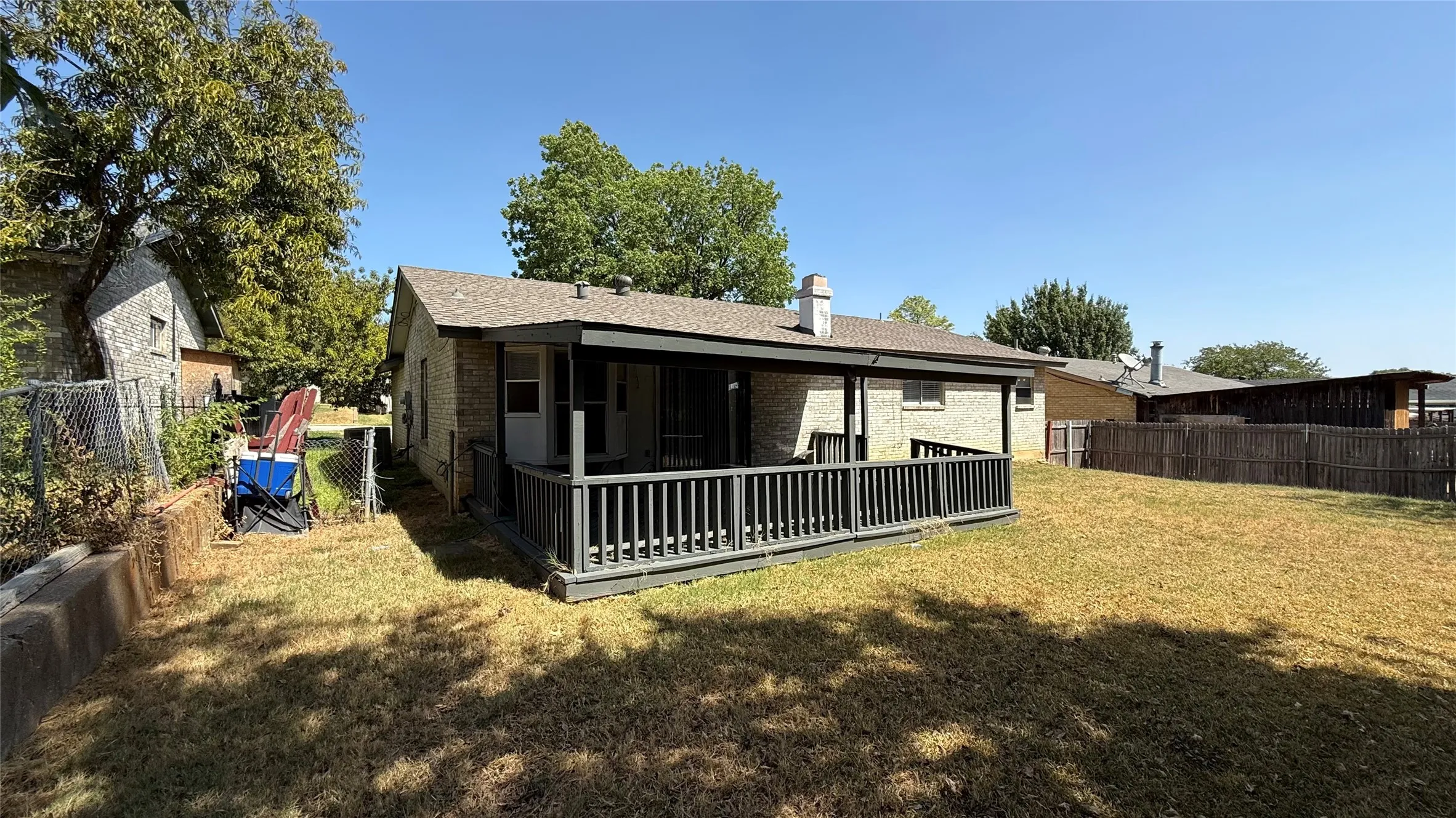 Rear exterior featuring a covered porch, wood deck with railing, and a fenced yard