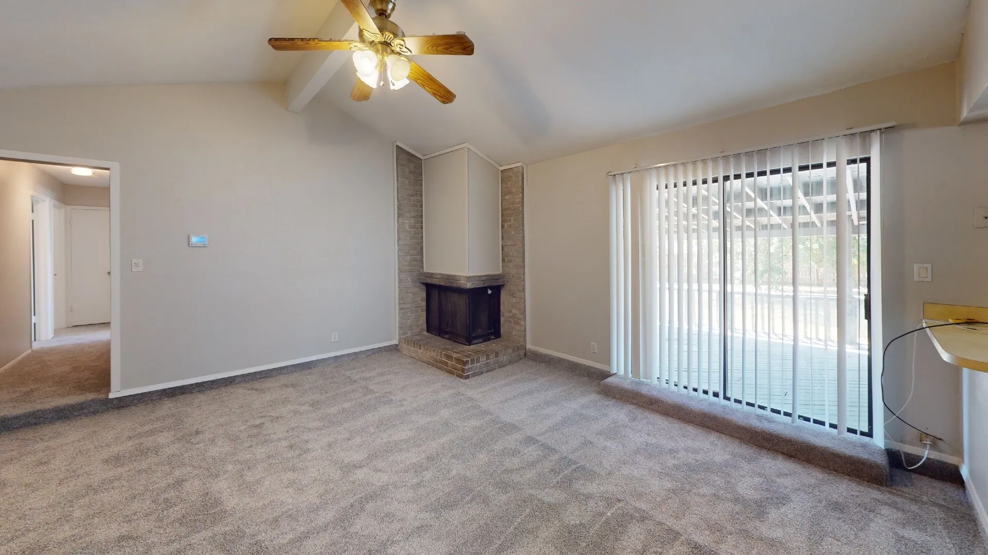 Vaulted ceiling with a ceiling fan, brick fireplace, and sliding glass door with vertical blinds